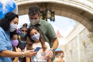A family wearing masks at Walt Disney World Resort while looking at a smartphone.