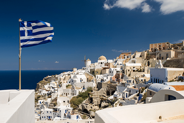 A flag of Greece waving above a beautiful city.